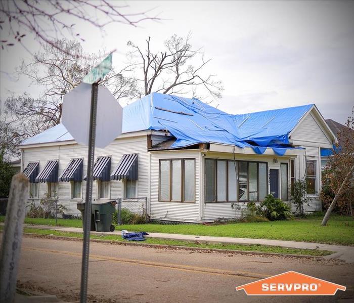 a home with a blue tarp secured to the damaged roof.